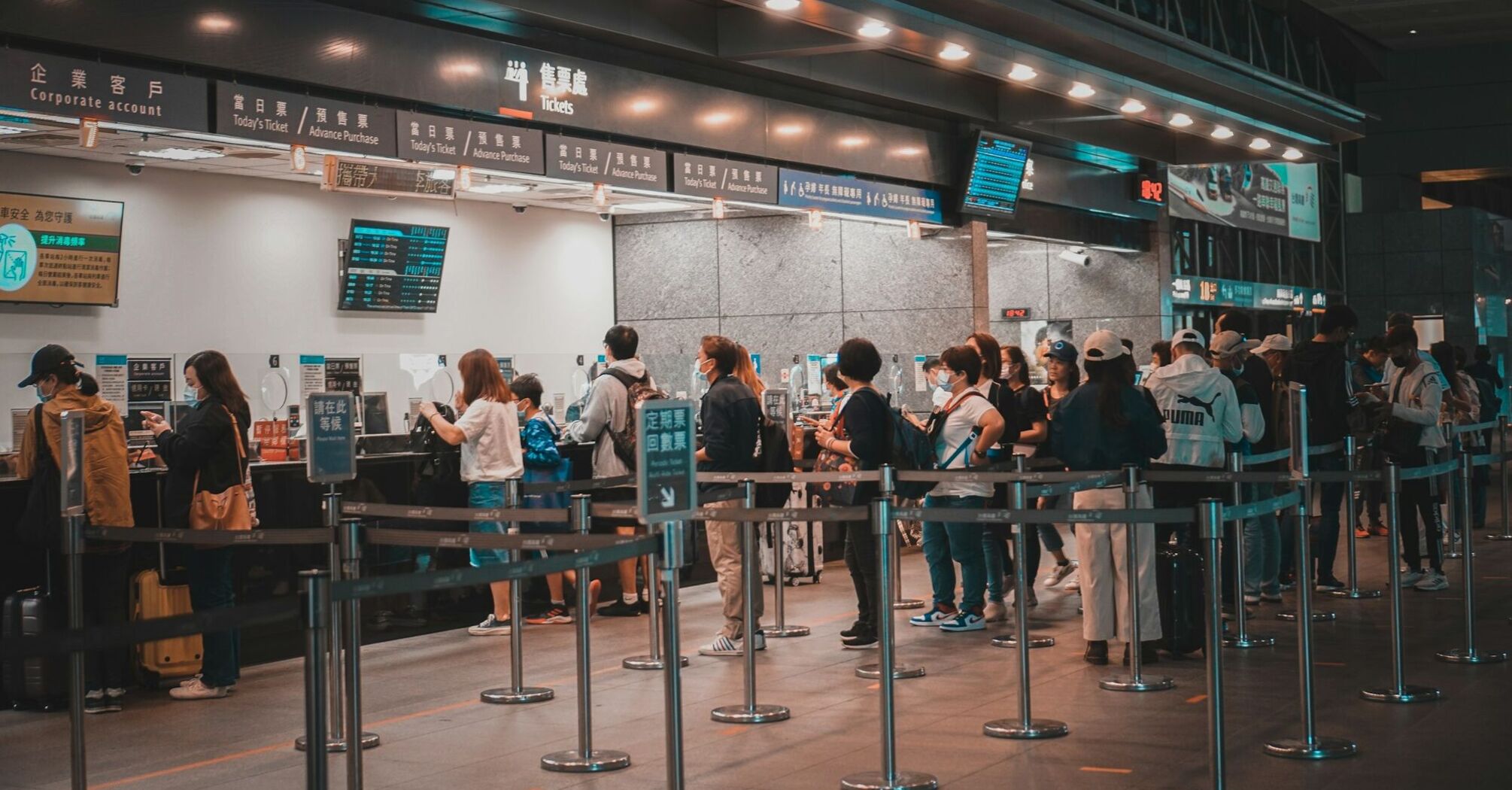 Travelers standing in line at a ticket counter with multiple service windows, some with longer lines than others 