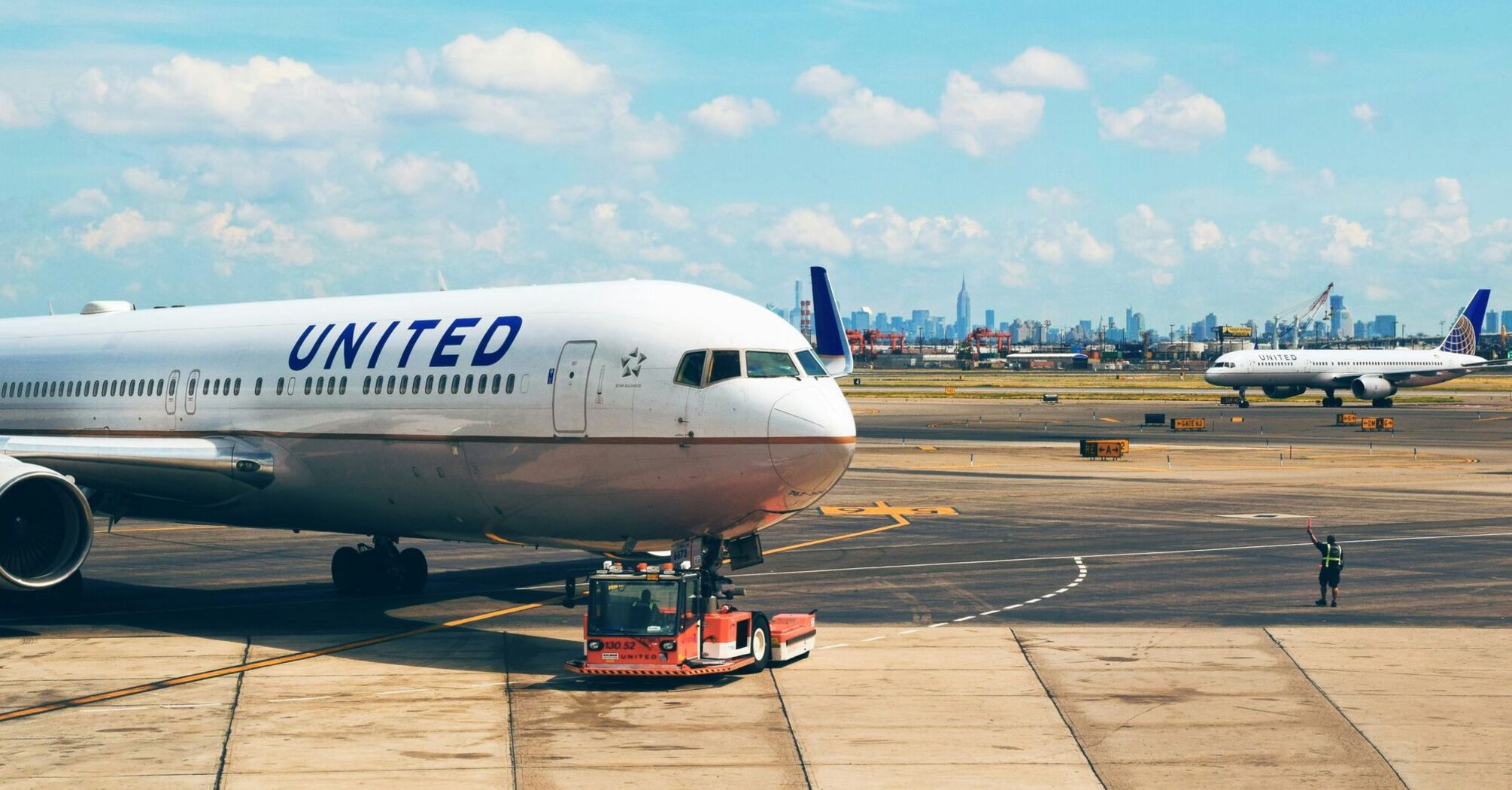 United Airlines aircraft being towed on the tarmac at an airport, with the city skyline in the background