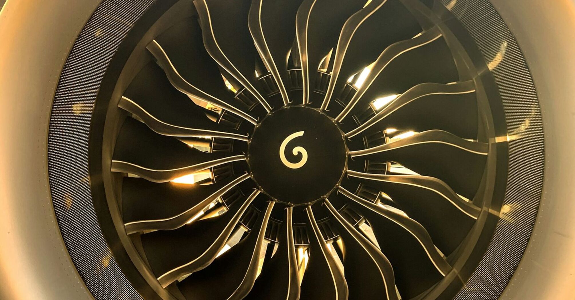 Close-up of a jet engine with distinctive fan blades and a central spinner on a tarmac at sunset 