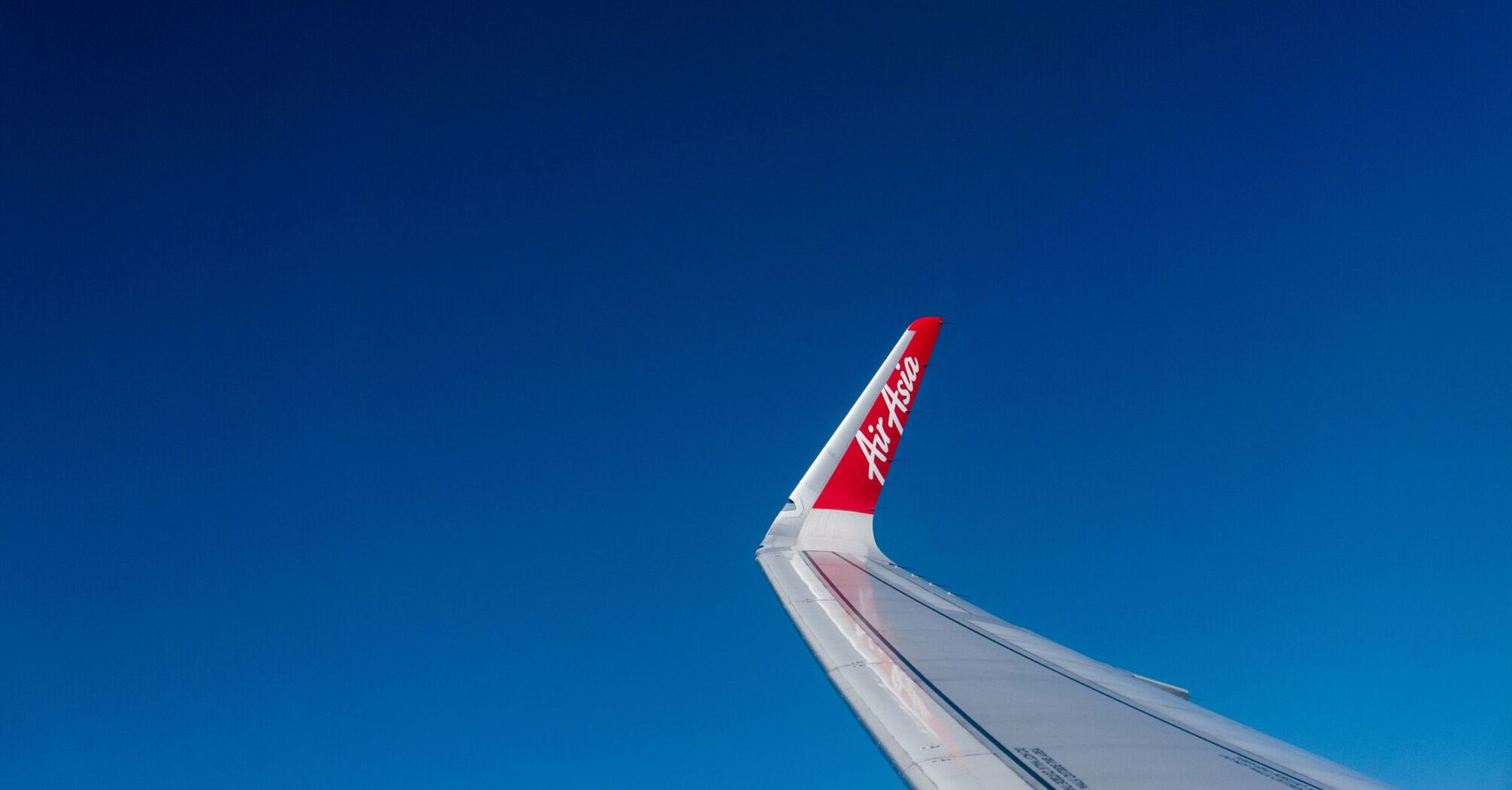 The wingtip of an AirAsia airplane with its distinctive red logo against a clear blue sky