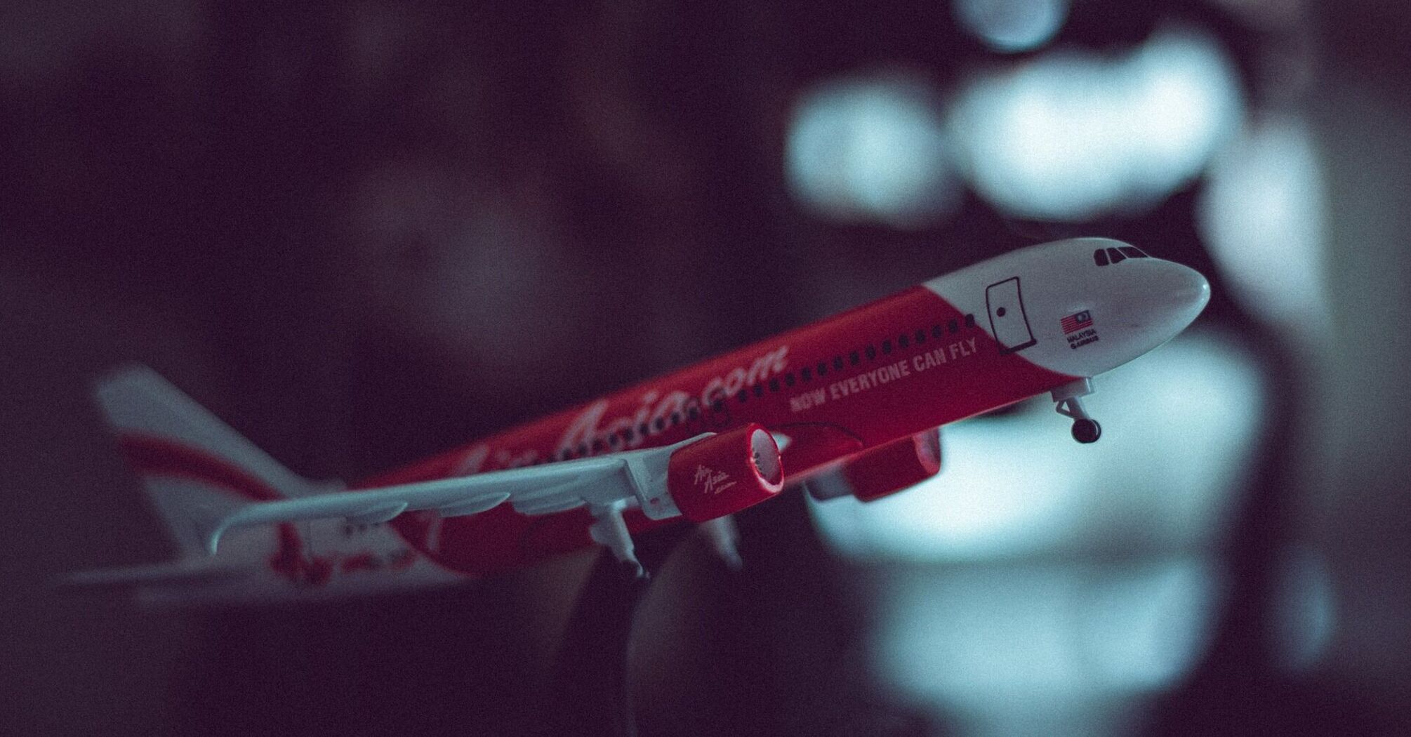 A model of a red AirAsia aircraft held in mid-air against a blurred background, showcasing the airline's livery and logo