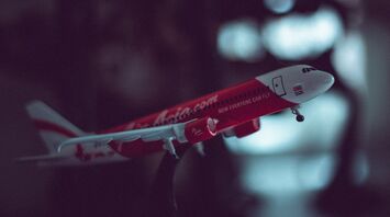 A model of a red AirAsia aircraft held in mid-air against a blurred background, showcasing the airline's livery and logo