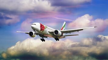 Emirates airplane in flight with a colorful rose design on its fuselage against a backdrop of a vibrant sky