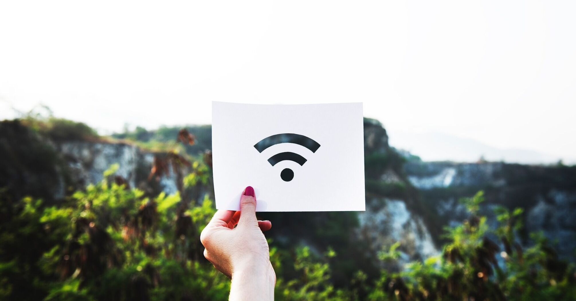 A person's hand holding up a paper with a Wi-Fi symbol on it against a blurred natural background