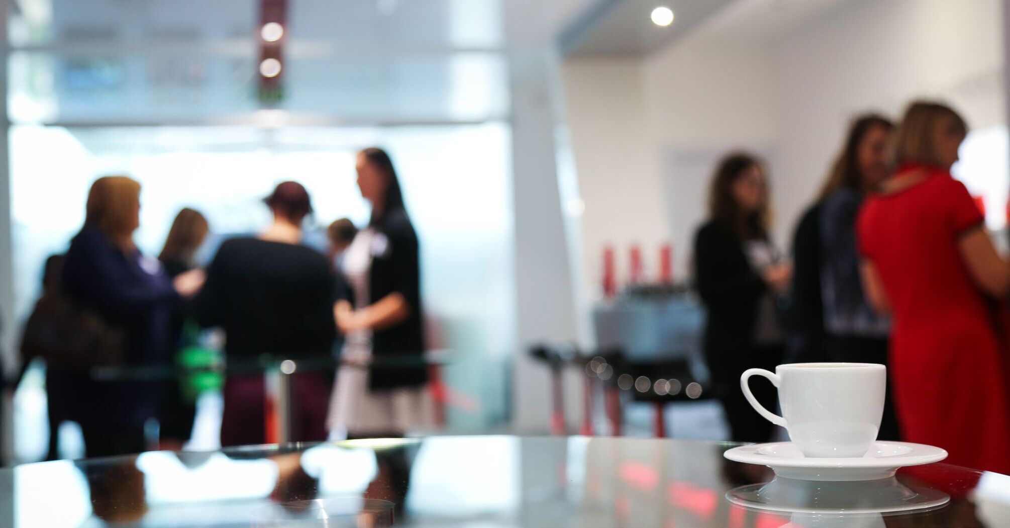 A coffee cup on a reflective surface with blurred background of people networking
