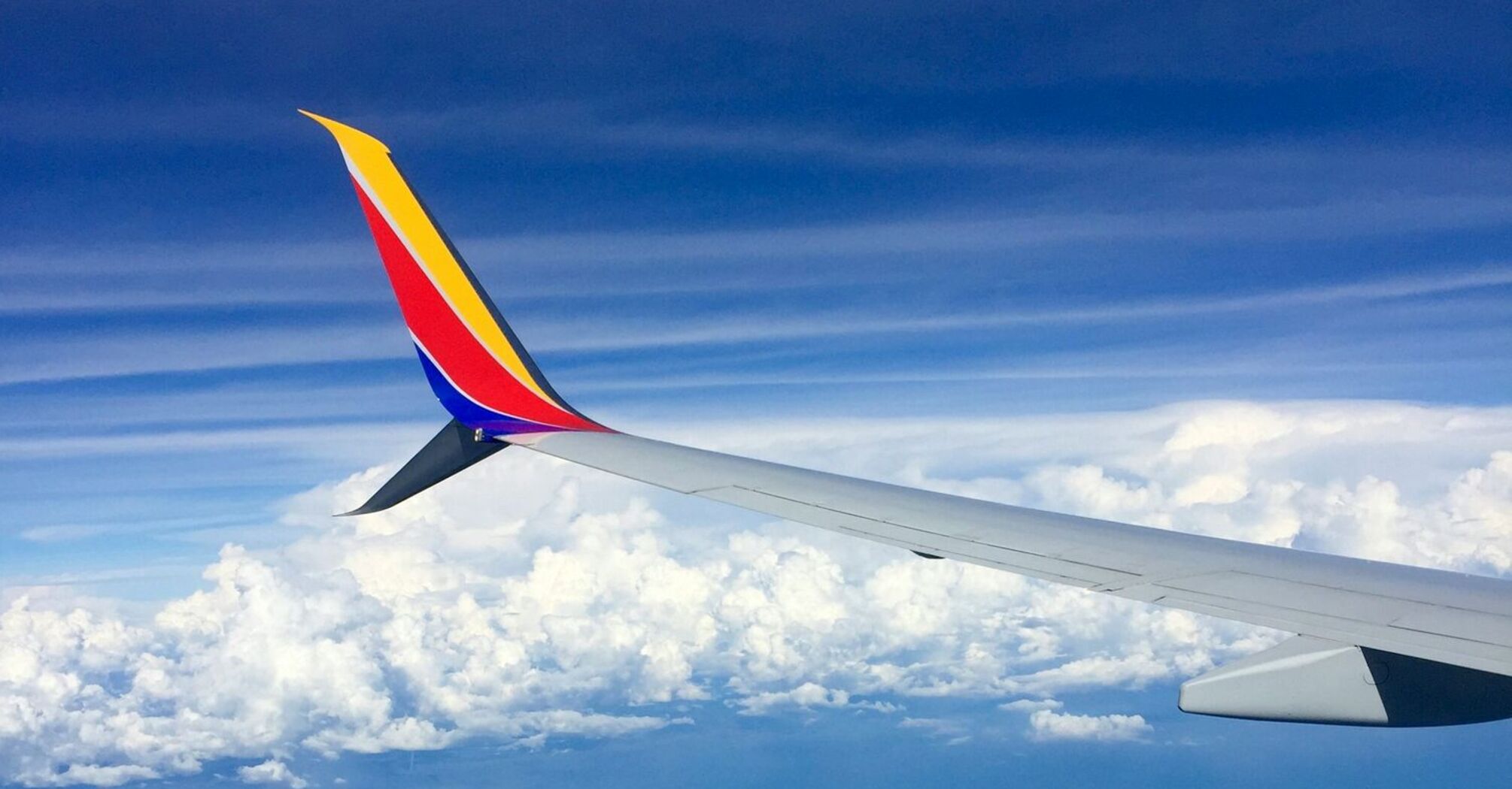 View of an airplane wing hovering above the clouds against a clear blue sky