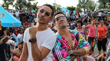 Two men enjoying an outdoor event, one in white shirt and sunglasses, the other in colorful attire