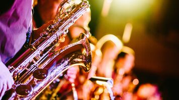 A close-up photo of saxophones being played on a brightly lit stage