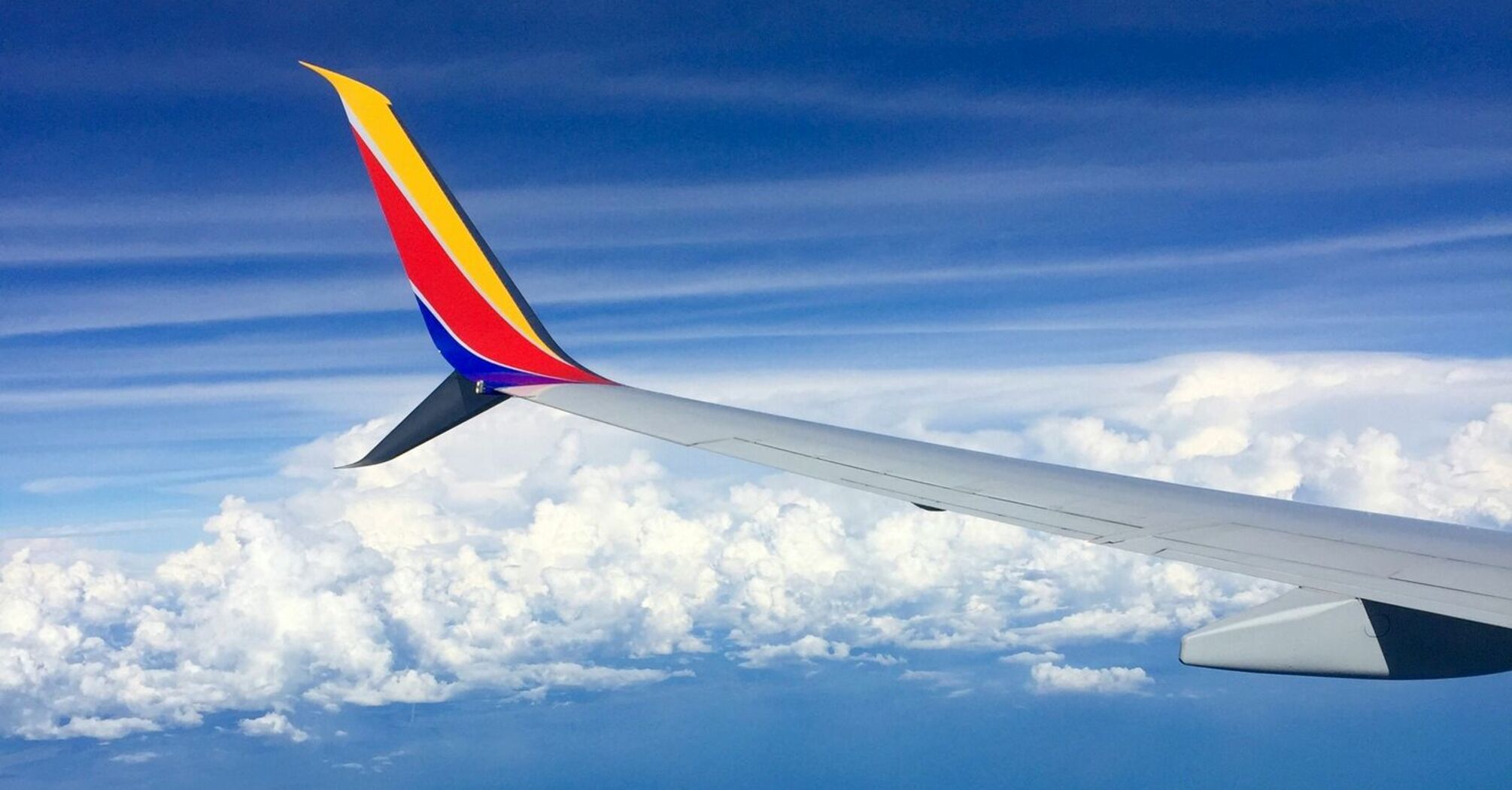 Wing of a Southwest Airlines plane in flight against a backdrop of blue sky and clouds