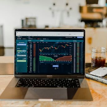 Laptop displaying financial trading graphs on a wooden table with a drink and smartphone