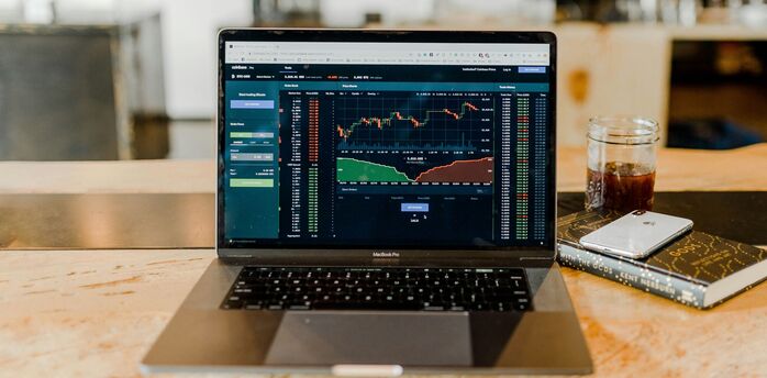 Laptop displaying financial trading graphs on a wooden table with a drink and smartphone