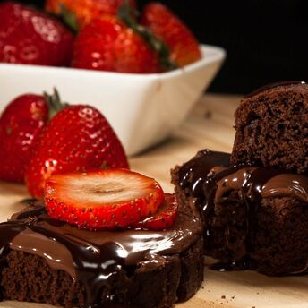 A chocolate cake with flowing chocolate ganache, served with sliced strawberries on a wooden board