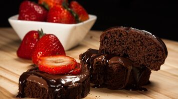 A chocolate cake with flowing chocolate ganache, served with sliced strawberries on a wooden board