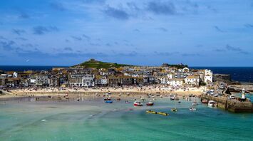 A bustling beach scene in St Ives, Cornwall, with colorful boats and a vibrant town backdrop