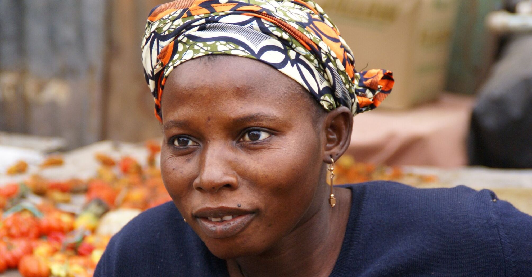 A Gambian woman at a market, wearing a headscarf and a navy blue top