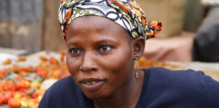 A Gambian woman at a market, wearing a headscarf and a navy blue top