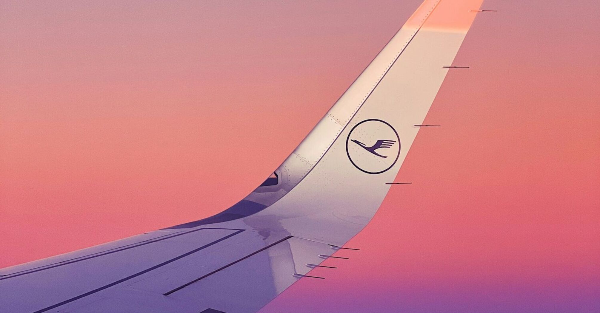 View of an airplane wing with the Lufthansa logo against a pink and purple sky