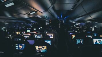 The interior of an airplane cabin with rows of seats, each with personal entertainment screens displaying various movies