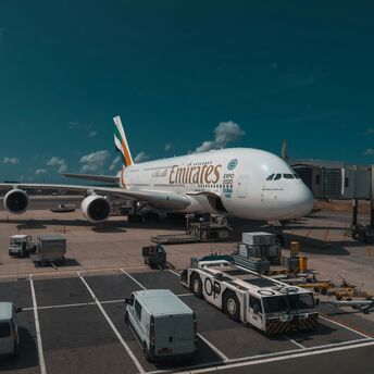An Emirates Airbus A380 aircraft parked at a gate with ground service equipment and vehicles around it under a partly cloudy sky