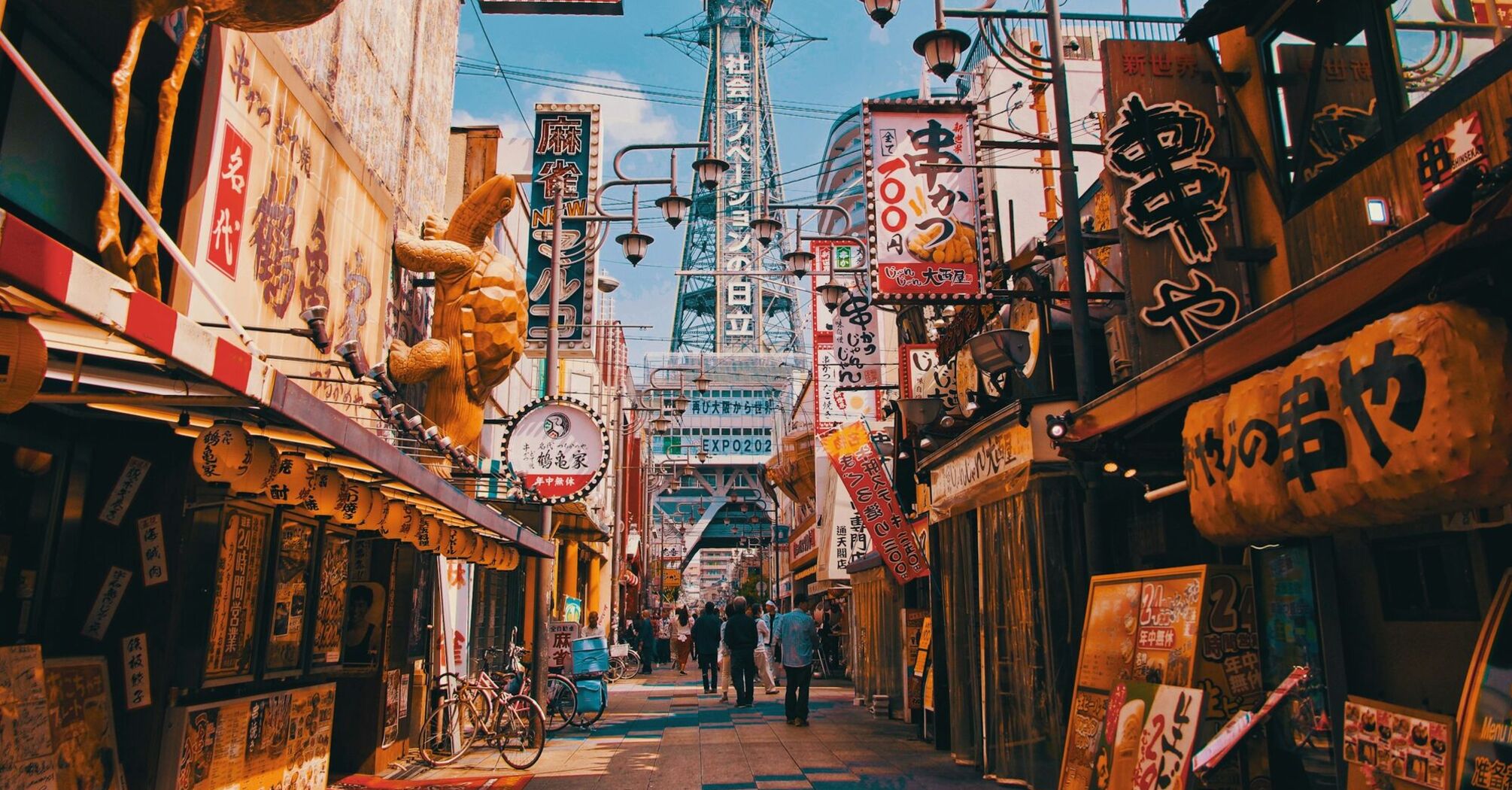 Colorful street in Osaka, Japan, with traditional signage and the iconic Tsutenkaku Tower in the background