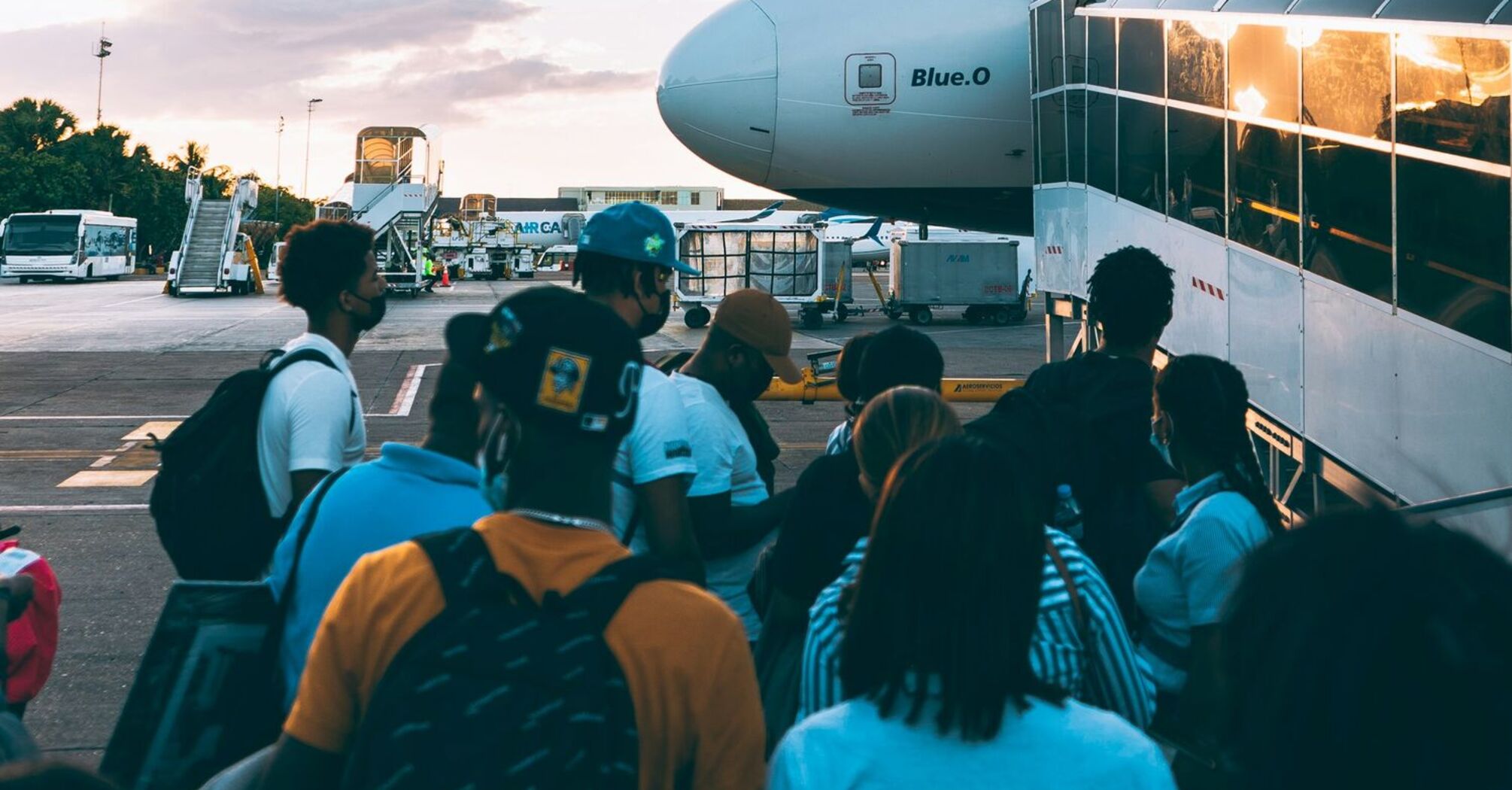 Passengers boarding an aircraft via a stairway on the tarmac during sunset