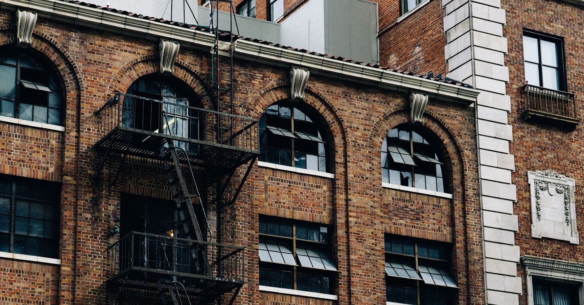 Old brick building with arched windows and an external metal fire escape staircase