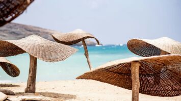 Brown wicker chair on white sand near body of water during daytime