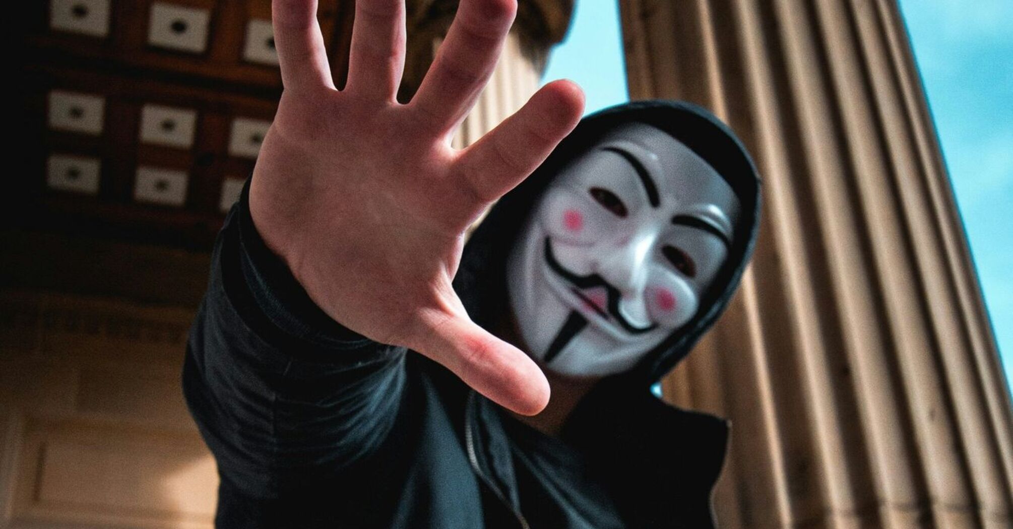 Person with a Guy Fawkes mask extending hand towards the camera