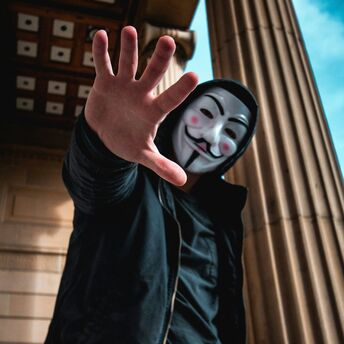Person with a Guy Fawkes mask extending hand towards the camera
