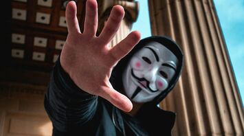 Person with a Guy Fawkes mask extending hand towards the camera