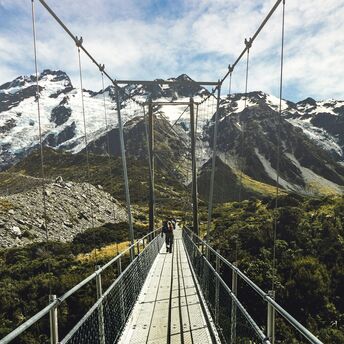 Hikers crossing a suspension bridge with mountainous backdrop