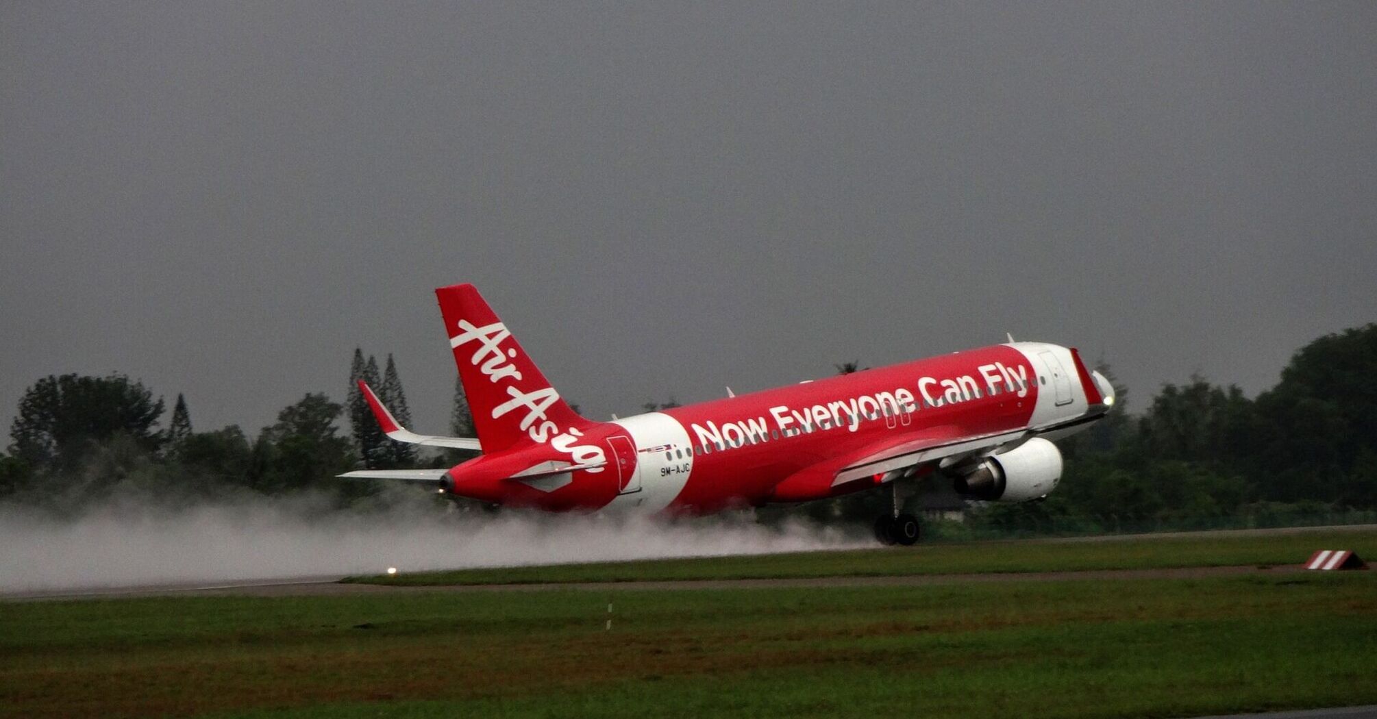 AirAsia airplane taking off on a rainy day with spray on the runway
