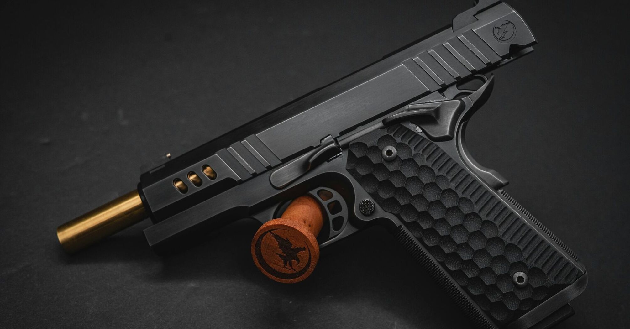 A black handgun with an embossed wooden grip rest on a dark background