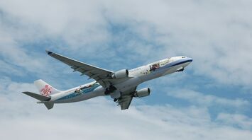 A large passenger jet flying through a cloudy blue sky