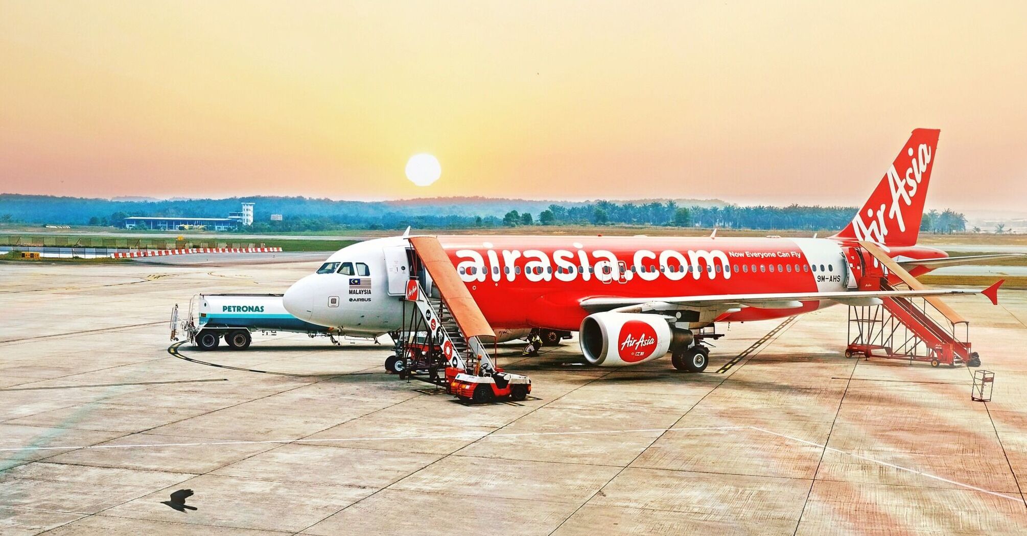 AirAsia airplane parked on the tarmac at sunrise, with passenger stair attached