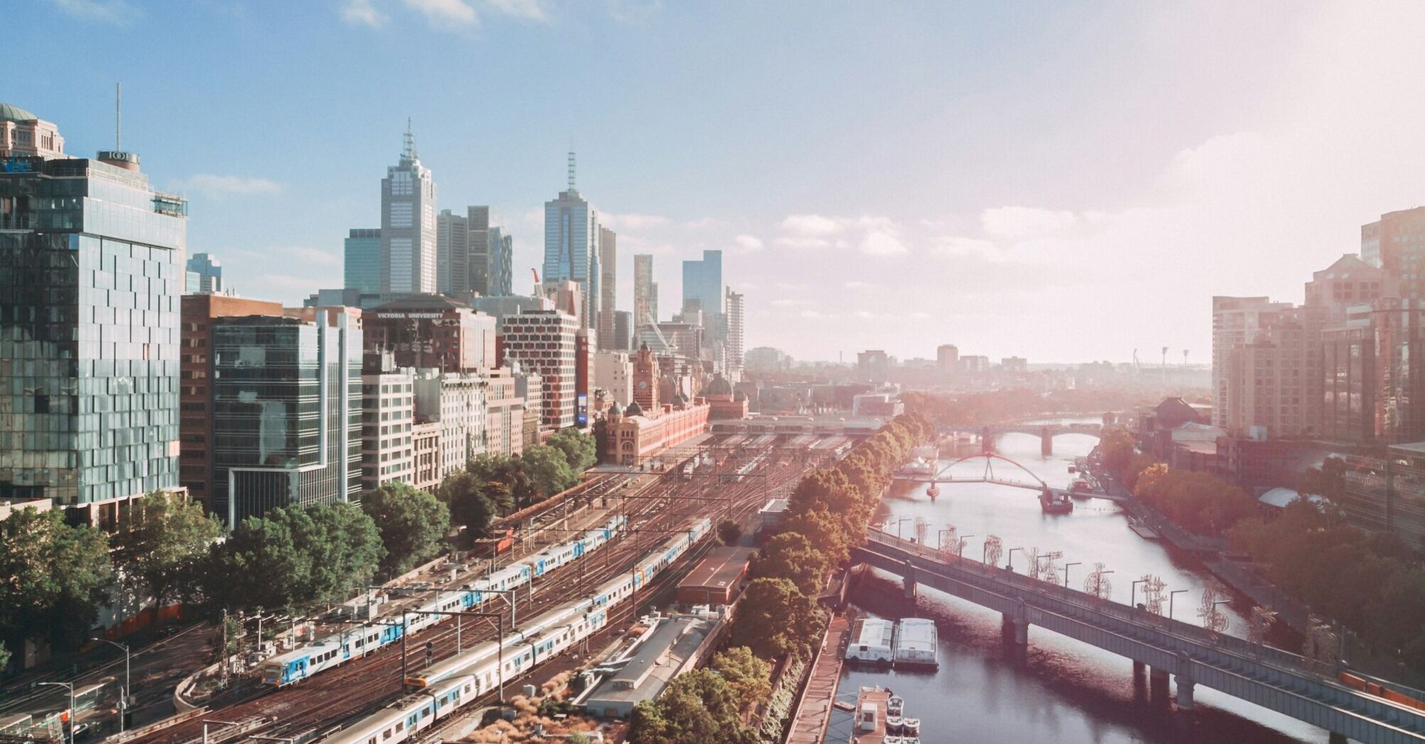 Aerial view of Melbourne cityscape with skyscrapers, the Yarra River, and trains on tracks on a sunny day