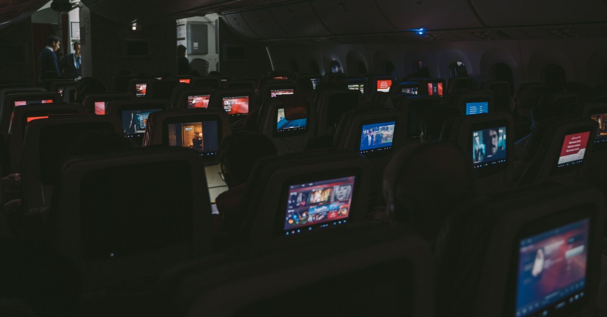 Cabin view of an airplane with seatback screens illuminated in a dimmed cabin