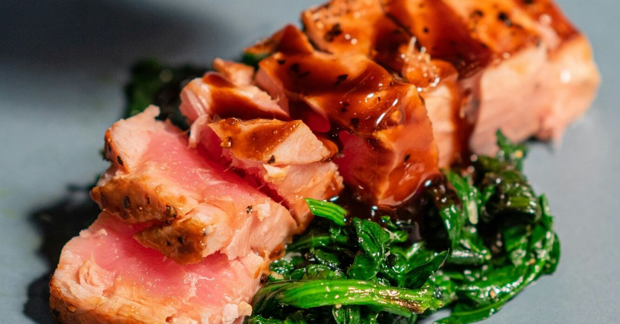 Sliced pink seared tuna on a blue plate with greens