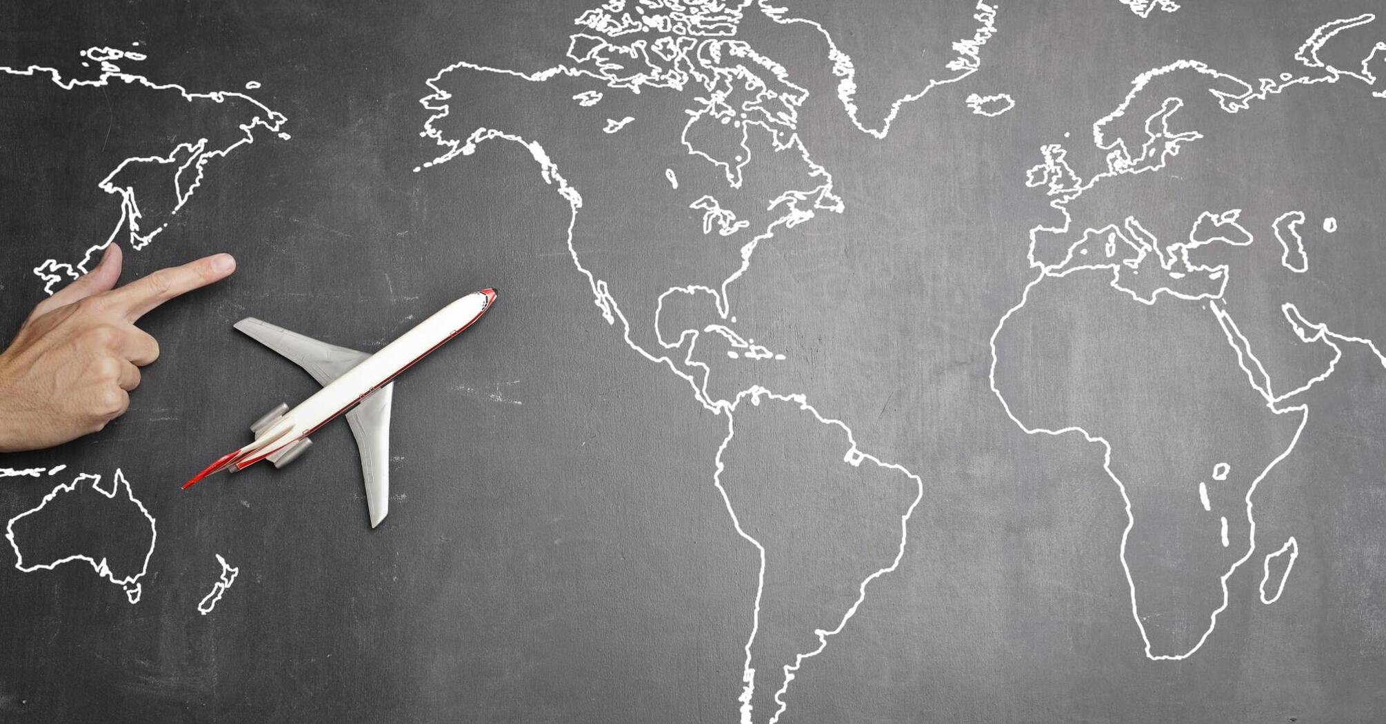 A world map outlined in white on a black chalkboard with a model airplane
