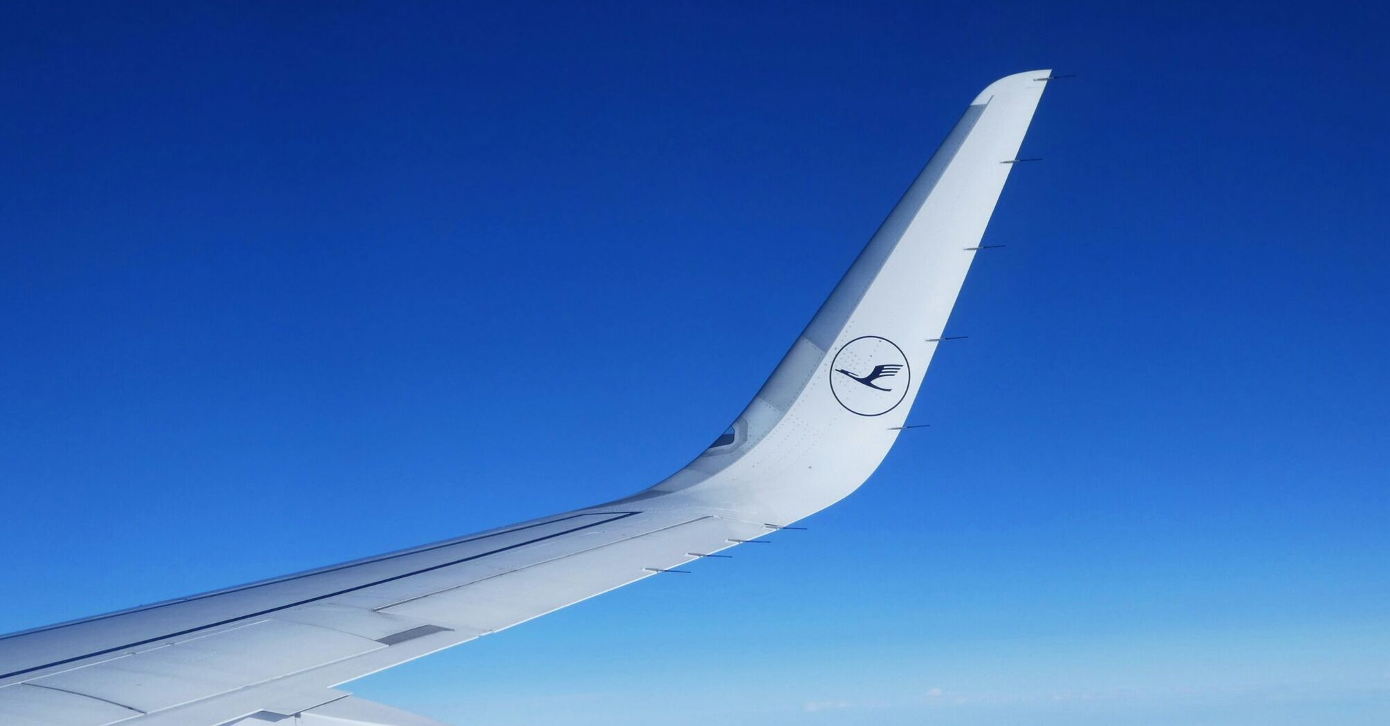 Wingtip of a Lufthansa airplane with the company's logo against a clear blue sky