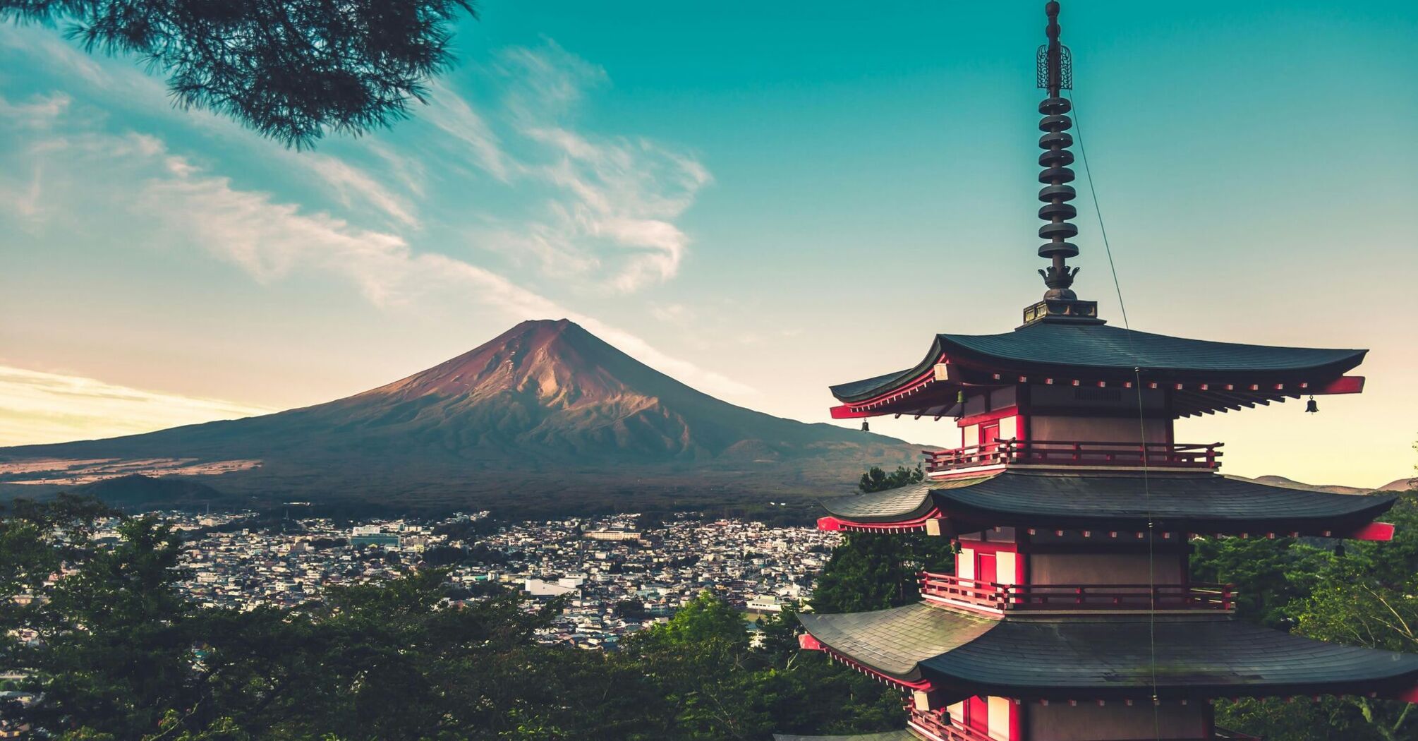 A pagoda with red and white tiers in the foreground with Mount Fuji and a town in the background at dusk