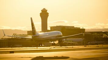 An Alaska Airlines plane landing at sunset with the airport control tower in the background
