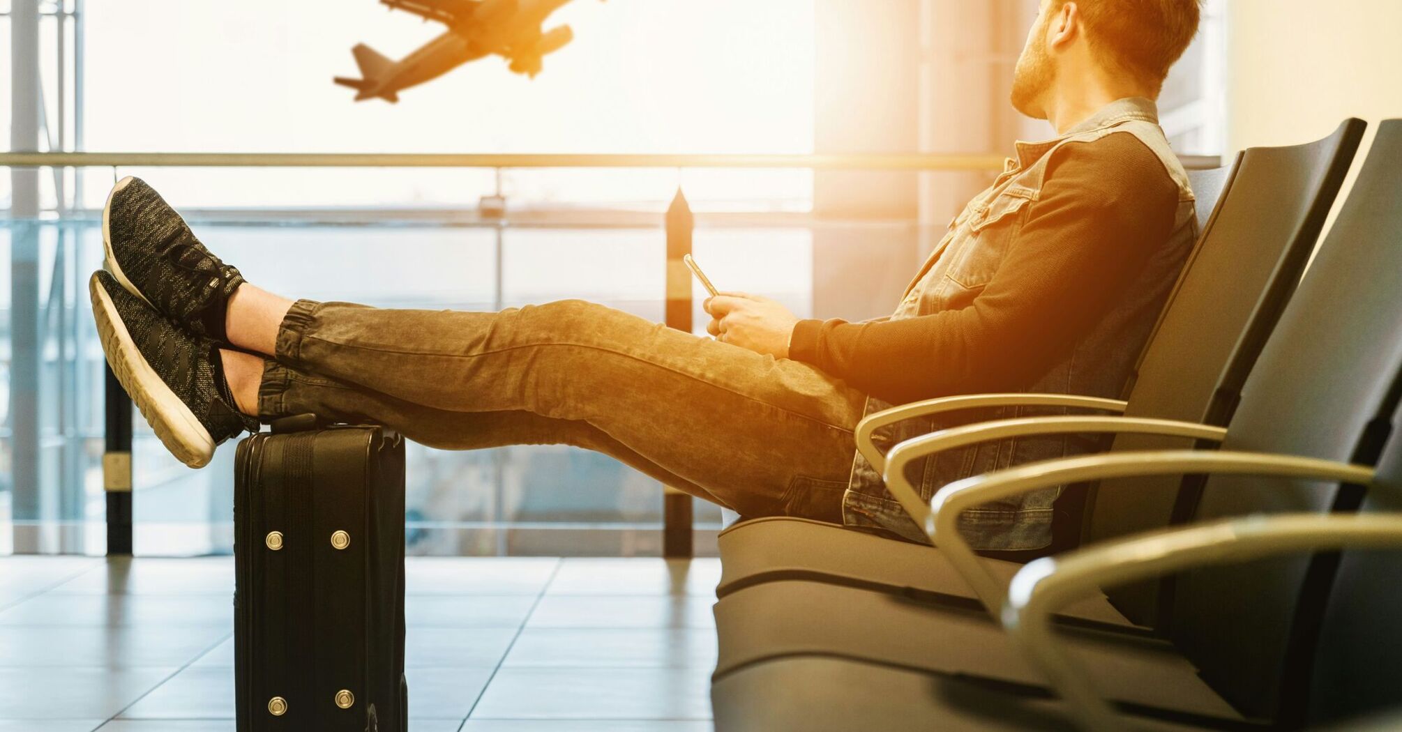Man sitting on gang chair with feet on luggage looking at airplane