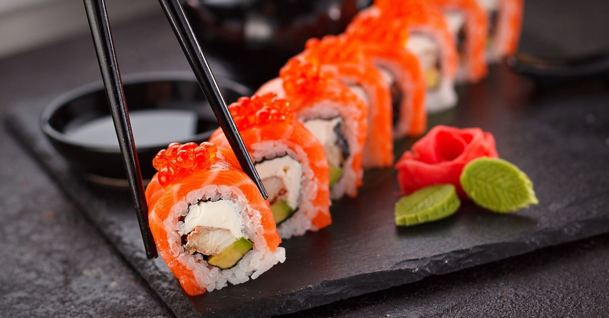 Sushi rolls with salmon and roe on a black slate with chopsticks