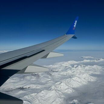 View from an airplane window showing a flydubai aircraft wing with clear blue skies