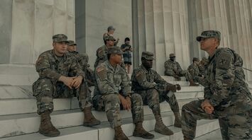 Group of U.S. Army soldiers in camouflage uniform sitting and standing on the steps of a monument