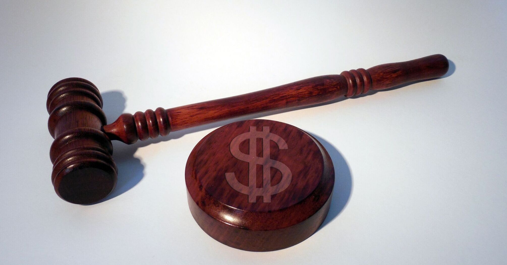 A wooden judge's gavel lying on top of a wooden block with a dollar sign symbol engraved on it 