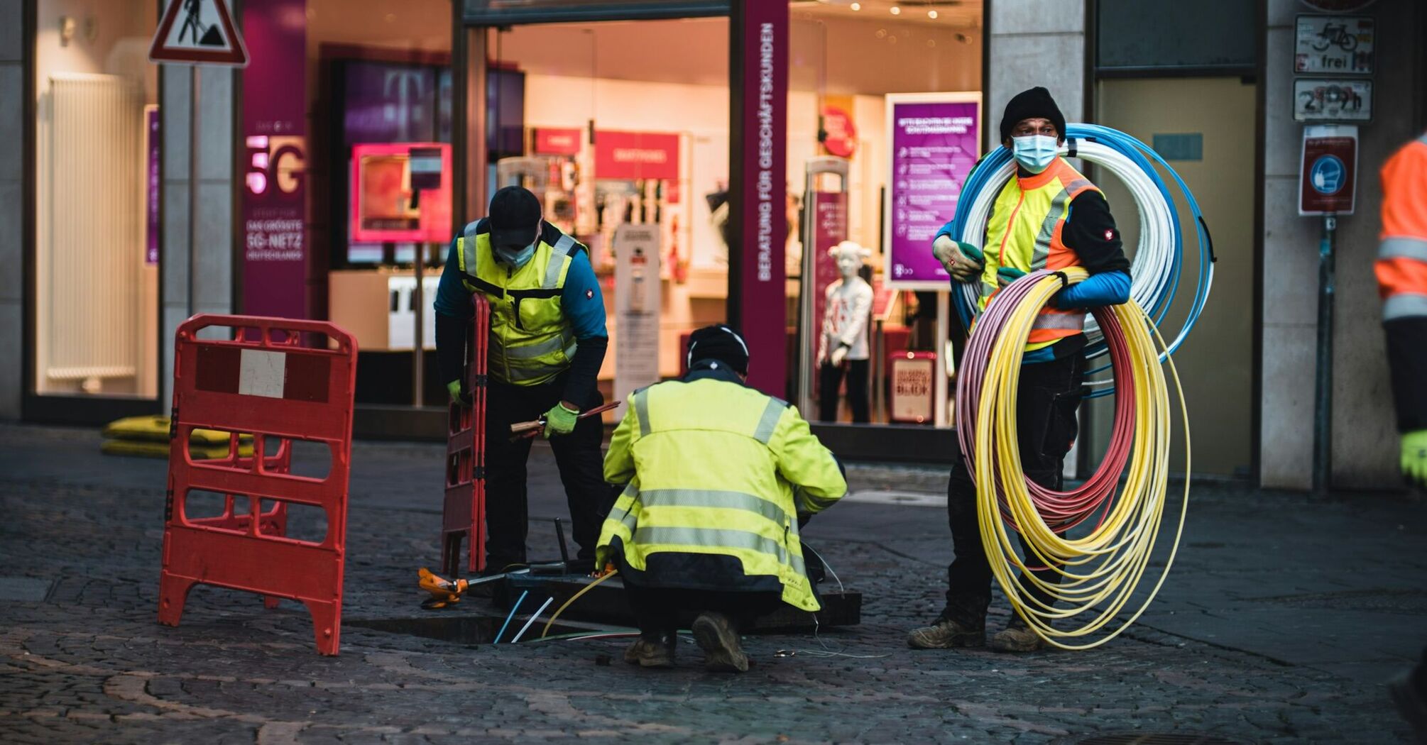 Workers in high-visibility jackets laying broadband cables on a city street 