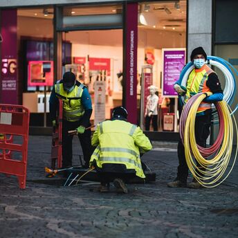 Workers in high-visibility jackets laying broadband cables on a city street 