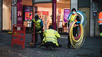 Workers in high-visibility jackets laying broadband cables on a city street